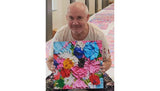 Damien Hirst holding a Cherry Blossom-inspired painting beside a table of similar colorful works